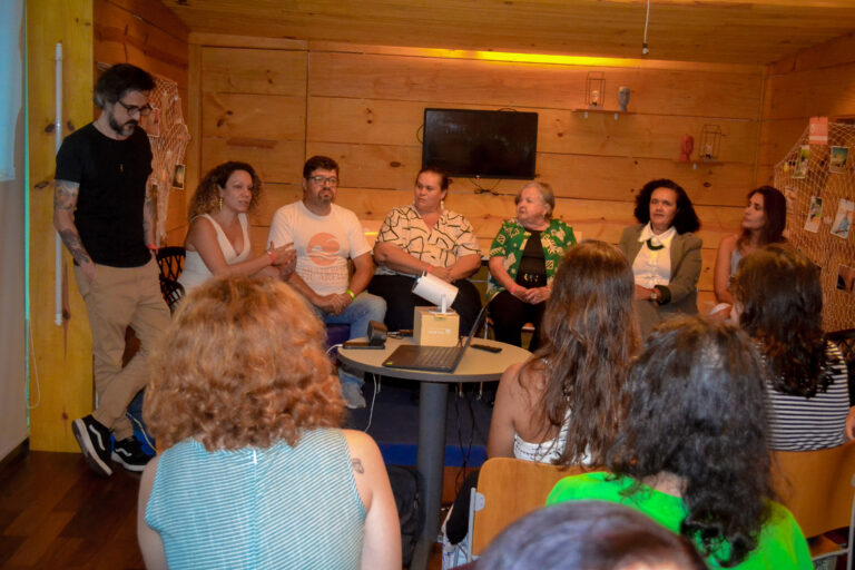 Participantes da Roda de Conversa e Oficina sendo vistos pela perspectiva da plateia, que aparece na cena